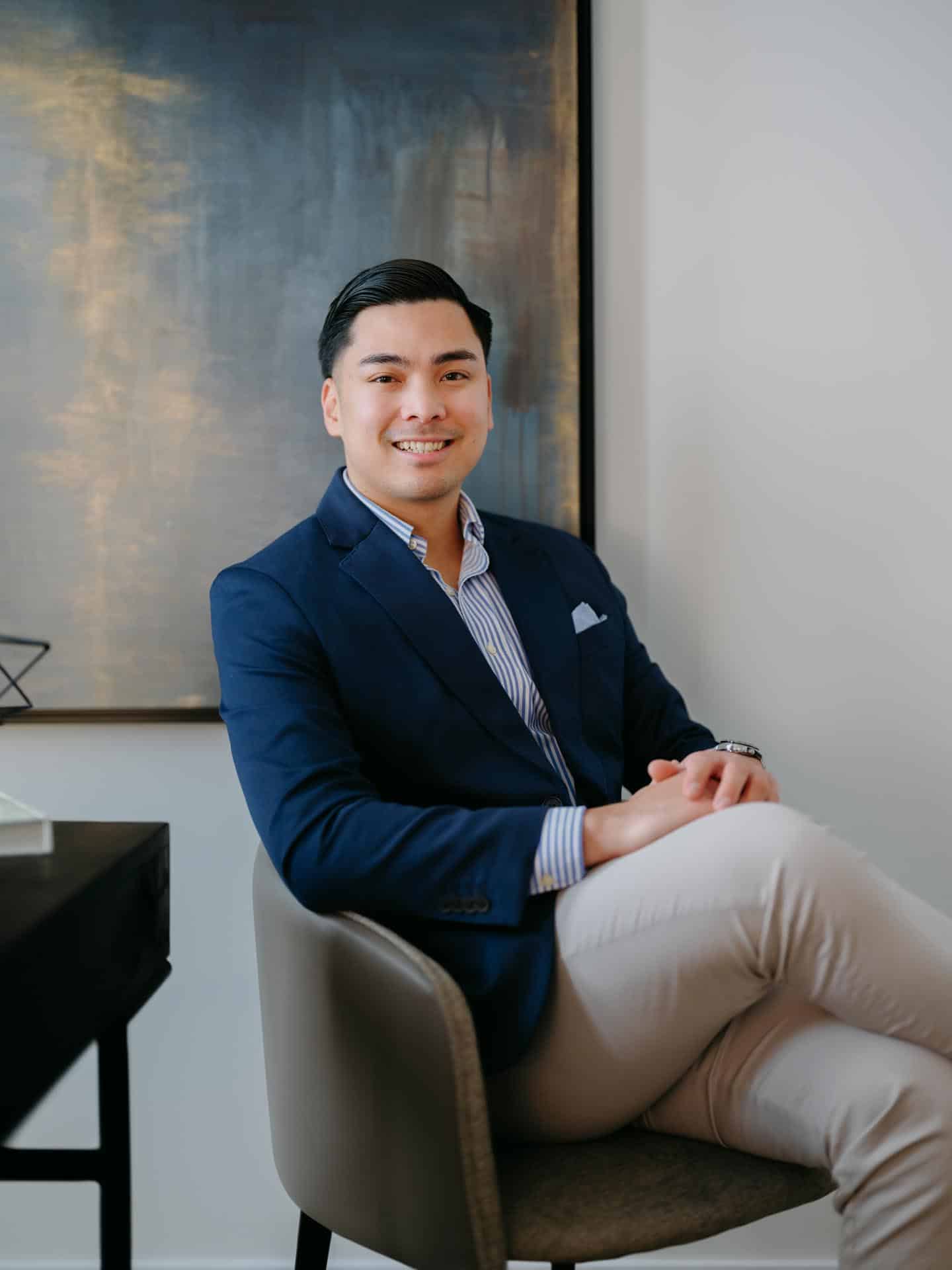 Mikee Canasa posing in a chair while explaining his Edmonton Real Estate Services and is ready to help you with selling a home in Edmonton.