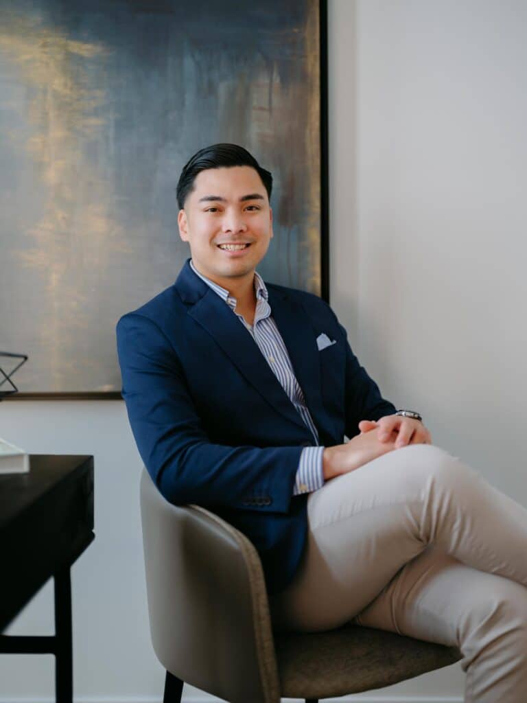 Mikee Canasa posing in a chair while explaining his Edmonton Real Estate Services and is ready to help you with selling a home in Edmonton.